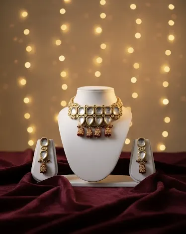 Gold kundan choker necklace and earrings set on maroon silk with golden bokeh lights for festive occasions